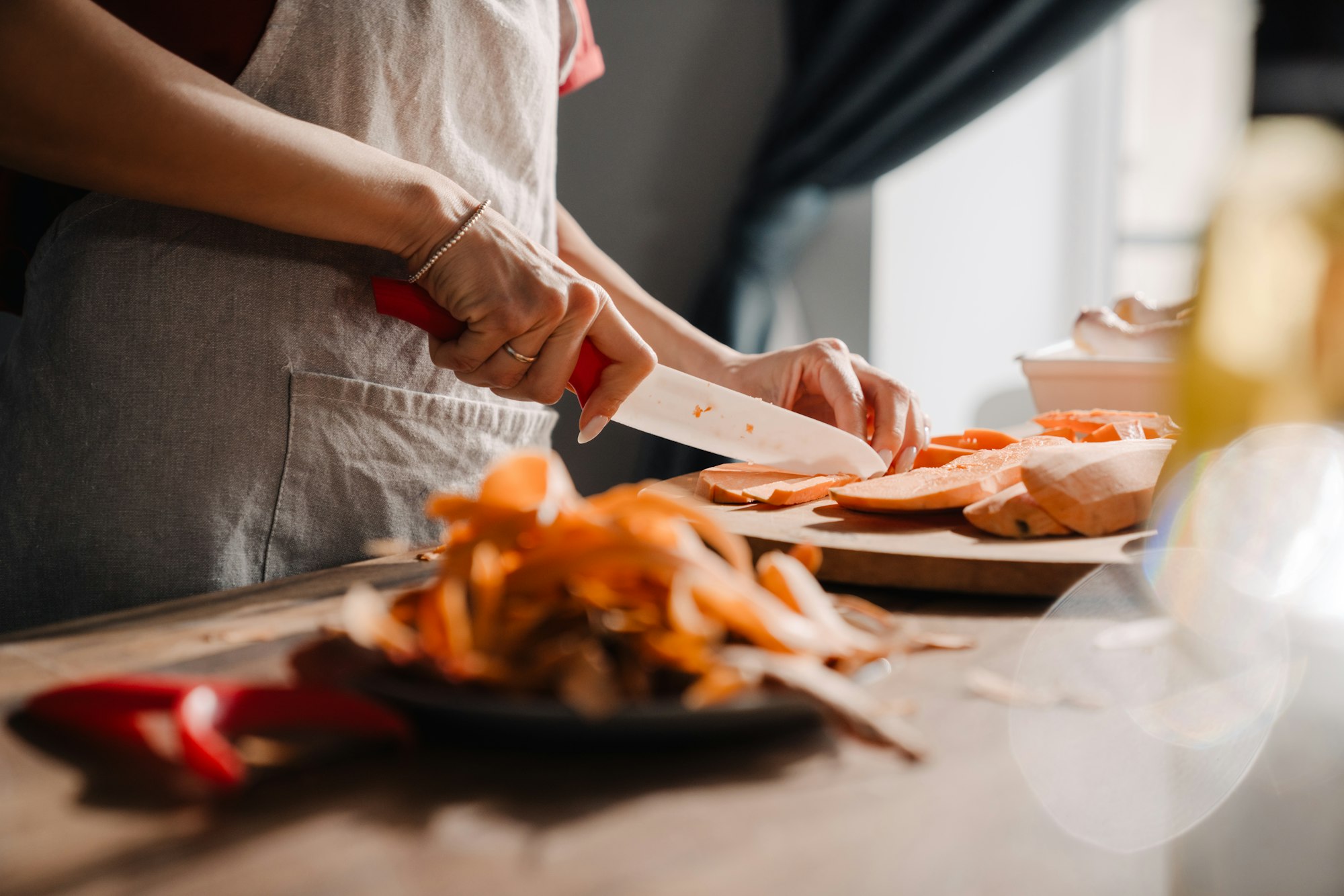 Young woman cutting sweet potato while cooking in kitchen